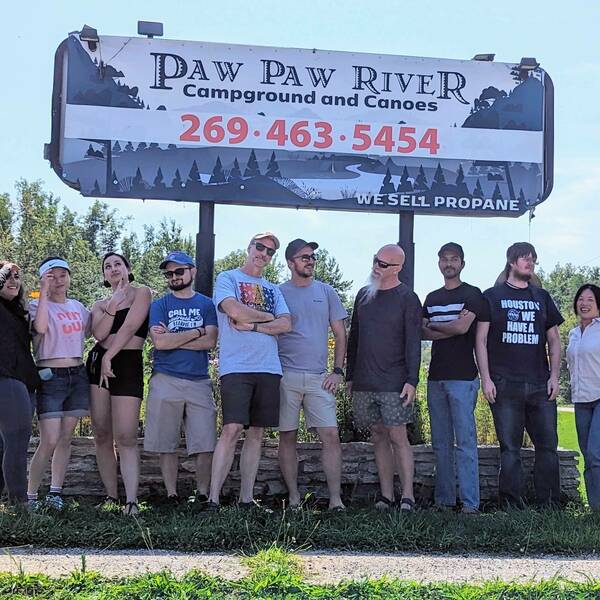 Lab members stand in front of Paw Paw River signage during canoe trip in 2023